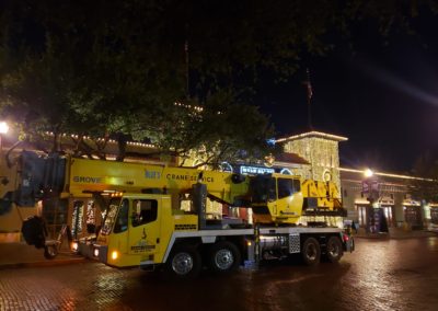 Blue's Hotshot Service crane on a road with festive lights behind it.