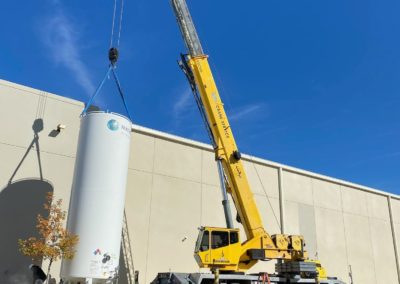 Blue's Crane Service crane placing a tank near a building.