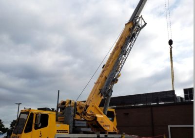 Blue's Crane Service crane stabilized and placing an HVAC unit on top of a building.