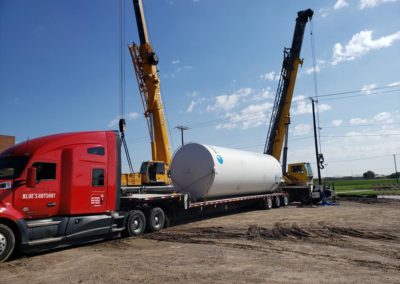 Blue's Crane Service crane behind one of Blue's Hotshot Service's truck and trailer getting ready to lift a tank.