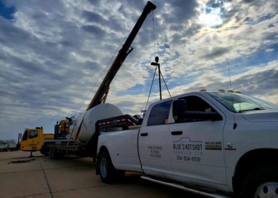 Blue's Crane Service crane lifting tanks off of a Blue's Hotshot Service flatbed trailer.