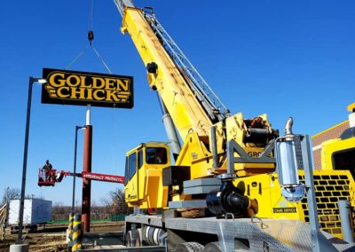 Side view of Blue's Crane Service crane placing a Golden Chick sign.