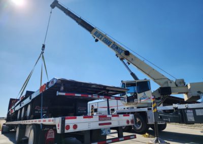 White Blue's Crane Service crane resetting a load on a flatbed trailer.